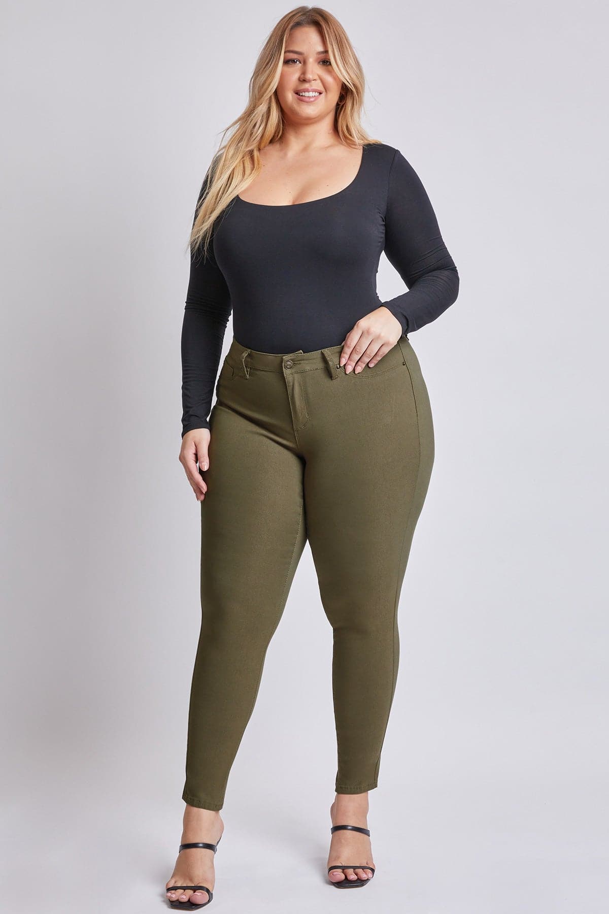 Woman wearing a black long-sleeve top and olive green pants on a white background