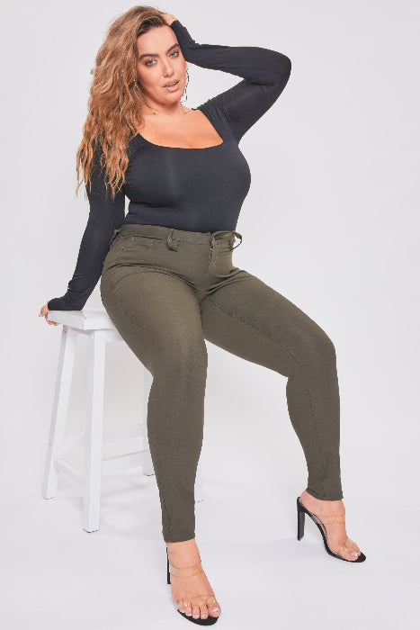 Woman sitting on a stool wearing a black top and green pants against a white background