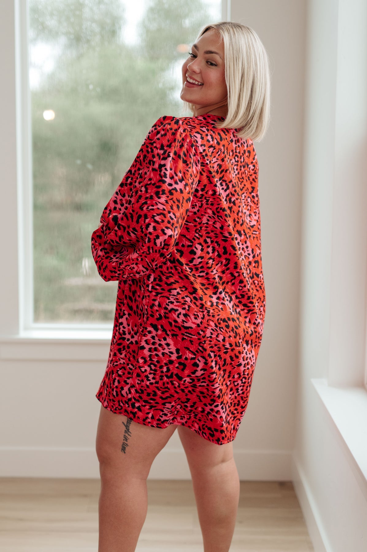 Woman wearing a red leopard print dress standing in a room with a window.