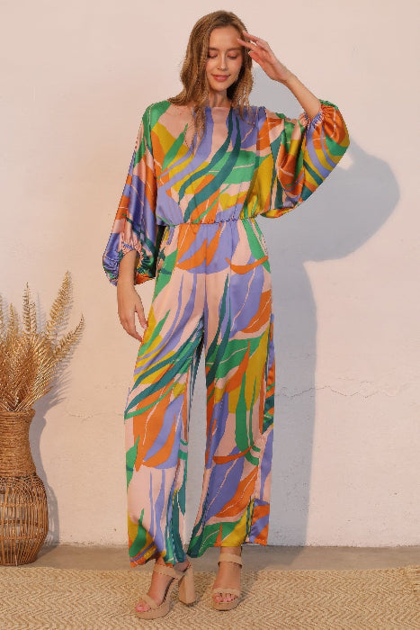Woman wearing a colorful blue patterned jumpsuit standing against a plain wall.