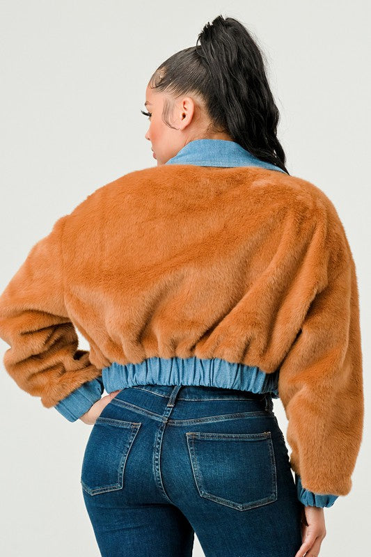 Person wearing a brown fuzzy jacket and blue jeans on a plain background