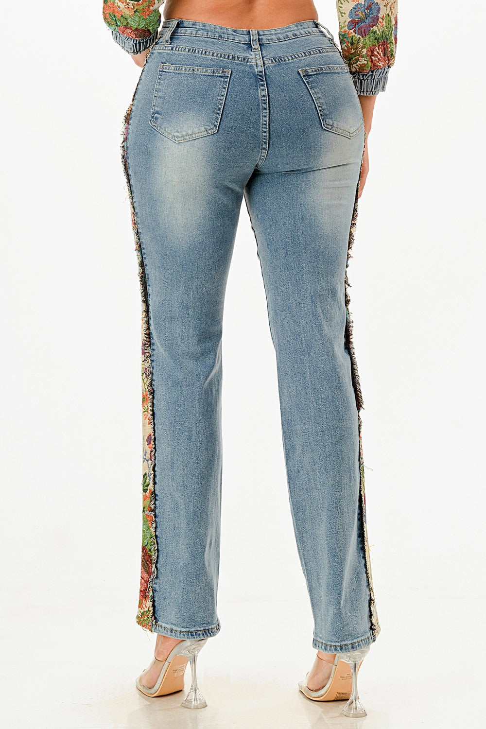 Blue jeans with floral side panels worn by a woman on a white background