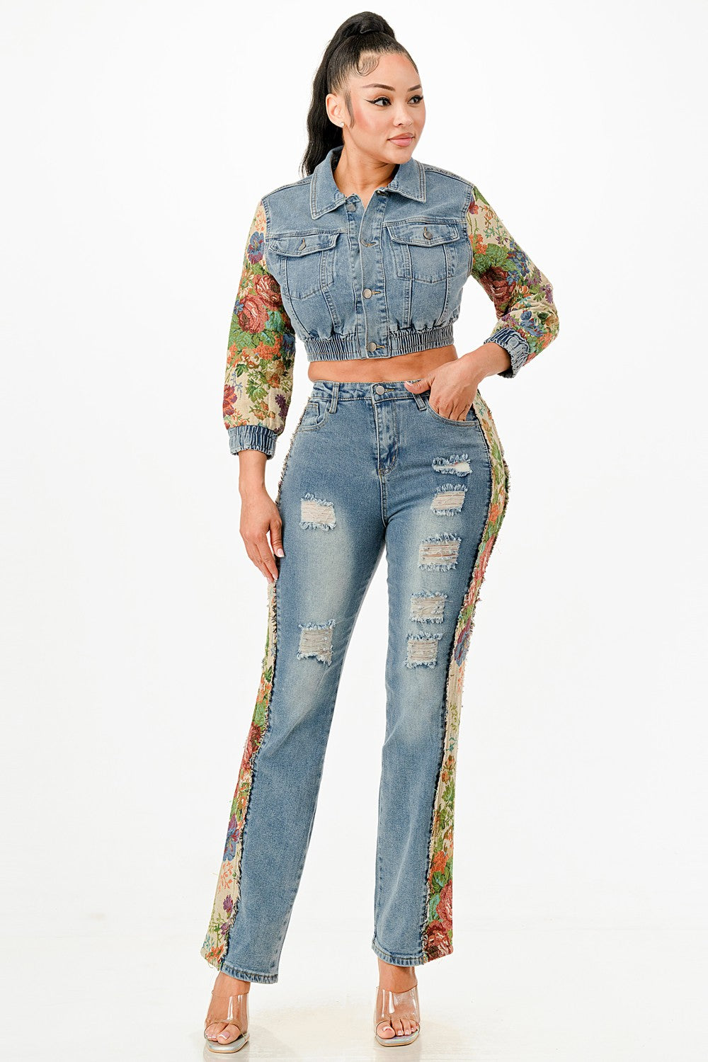 Woman wearing a denim jacket with floral sleeves and matching jeans on a white background