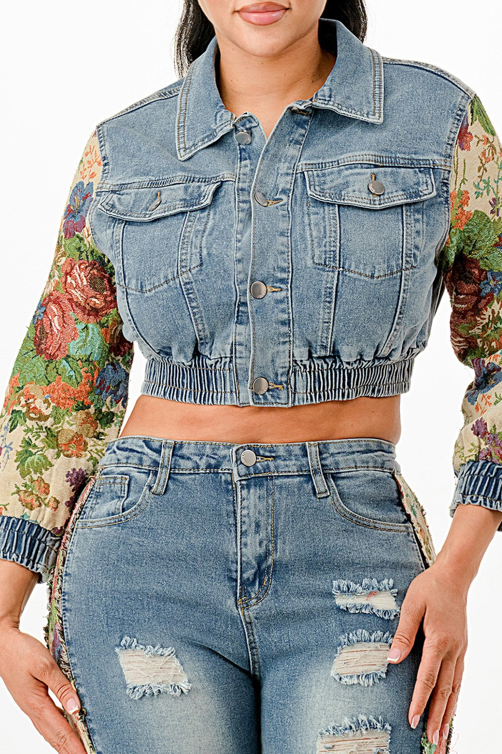 Close up ot woman wearing a denim jacket with floral sleeves and distressed denim jeans