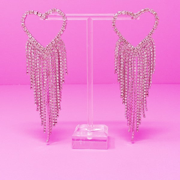 Heart-shaped earrings with dangling crystals on a pink background