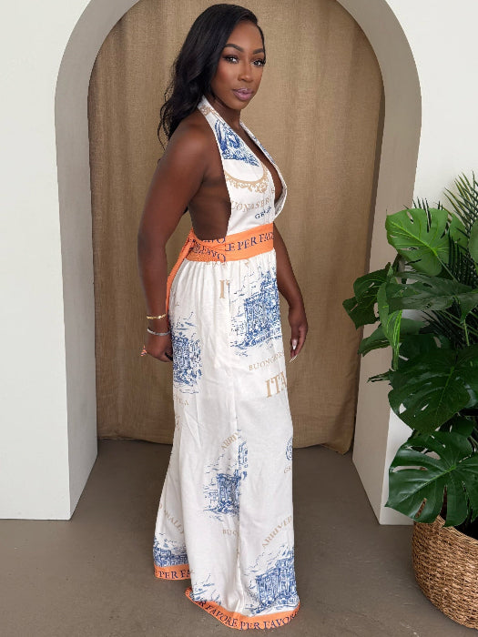 Woman wearing a patterned jumpsuit standing in a room with a plant.
