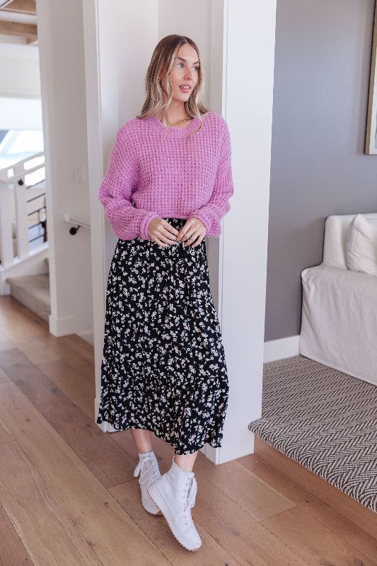 Woman wearing a pink checkered sweater and black floral skirt indoors.