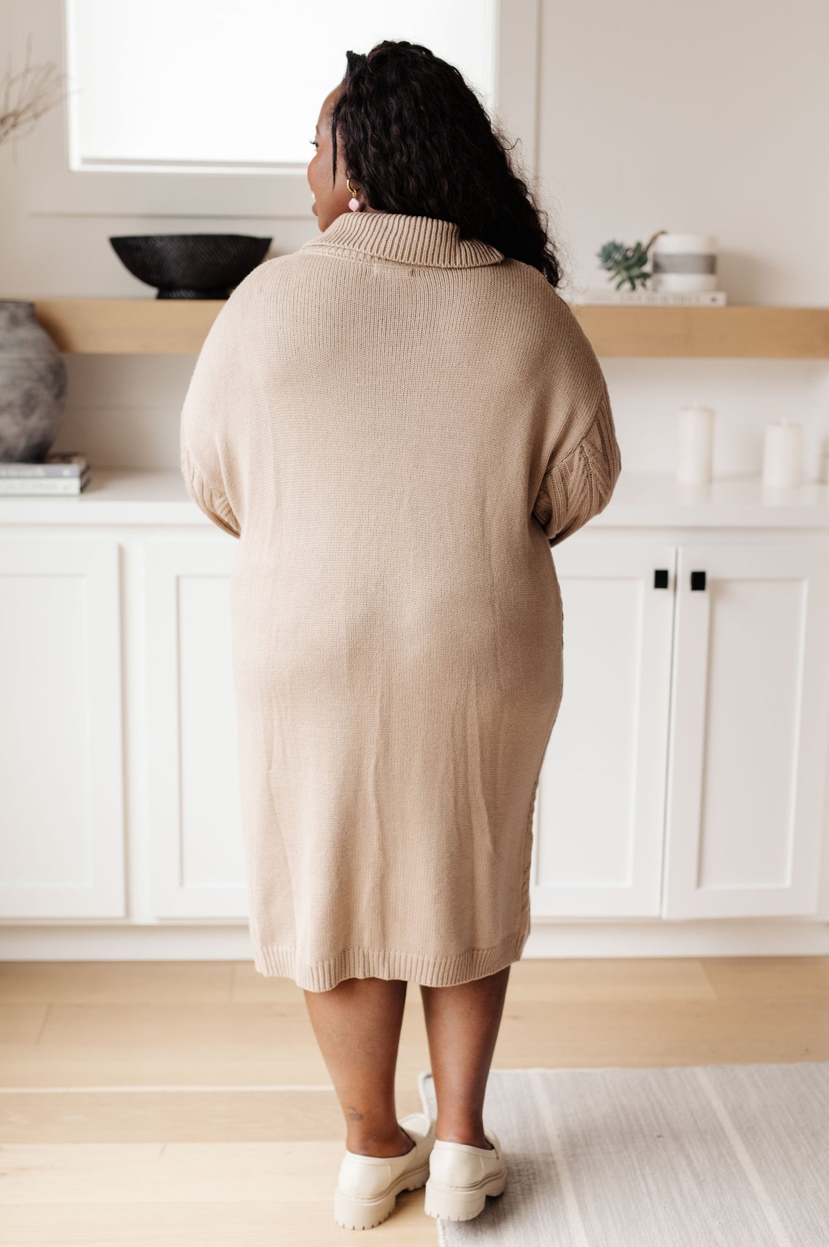Person wearing a beige sweater standing in a kitchen.