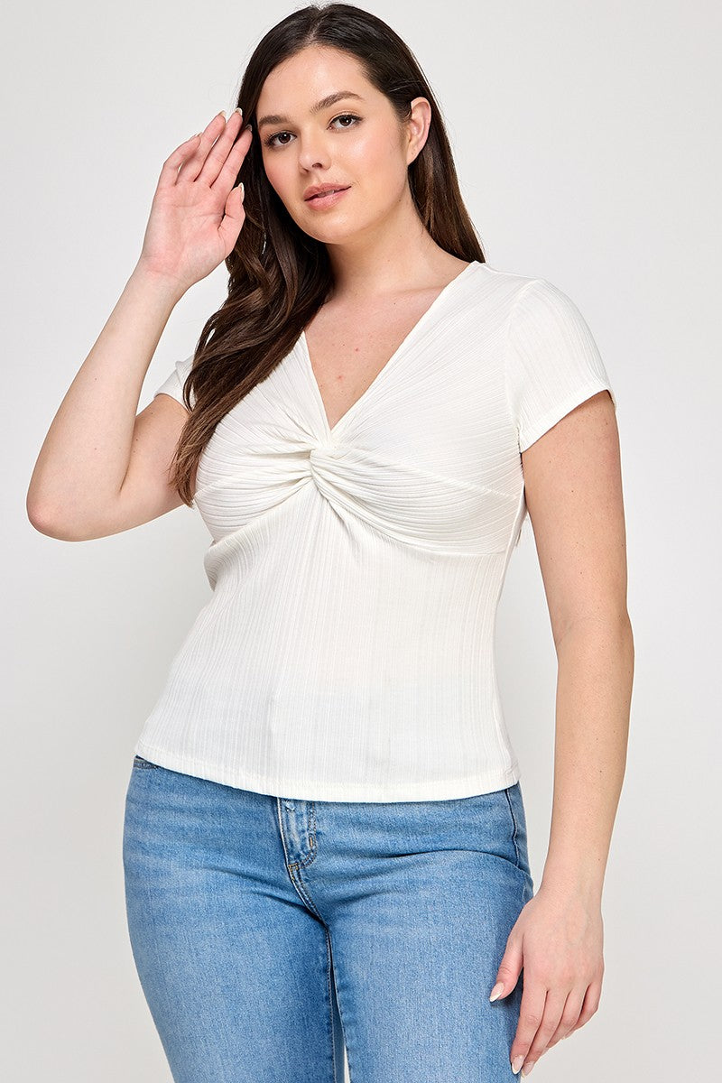 Woman wearing a white top with a ruched design and blue jeans on a plain background