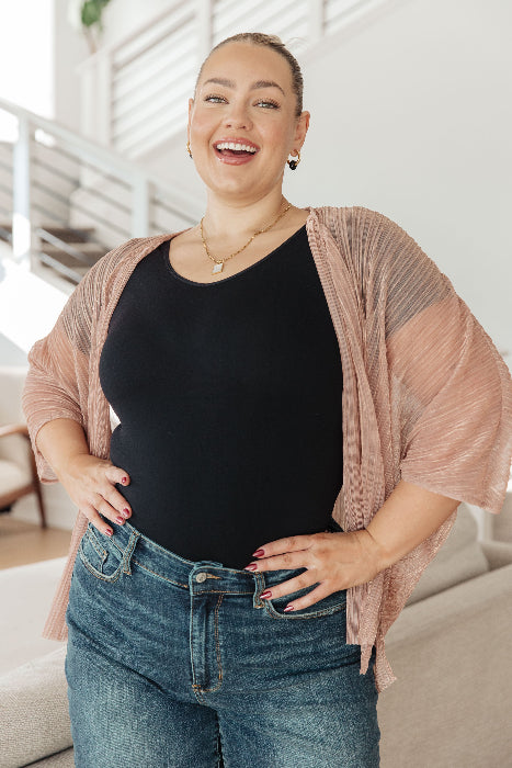 Woman wearing a black top and blue jeans with a pink cardigan indoors.
