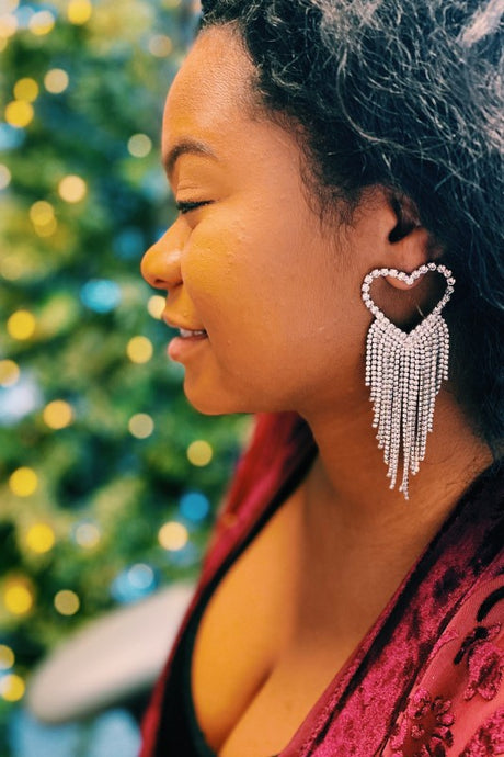 Woman wearing a heart-shaped earring with a Christmas tree in the background