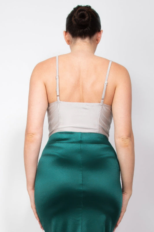 Back view of a woman wearing a silver bodysuit and green skirt on a plain background
