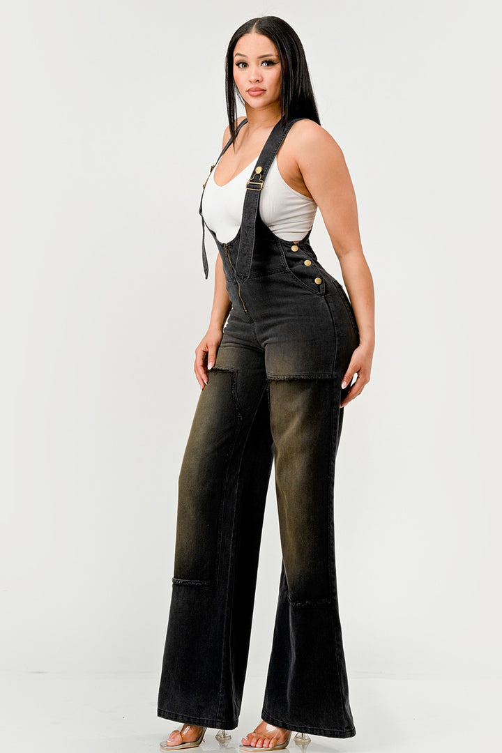 Woman wearing black overalls with a white top on a plain background