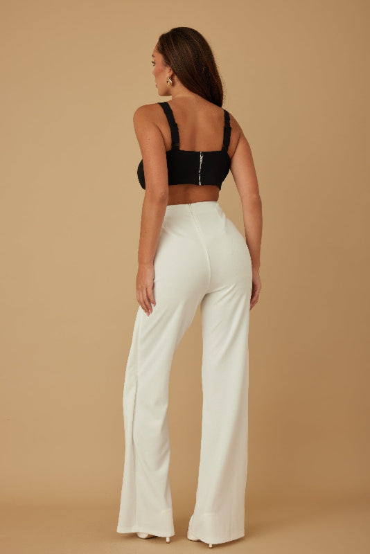 Woman wearing a black crop top jumpsuit with white high-waisted bottom on a beige background