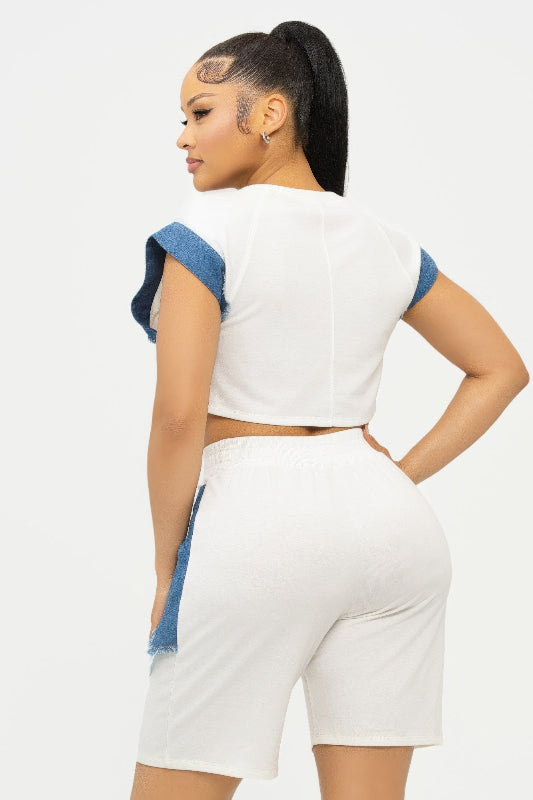 back view of Woman wearing a white crop top and shorts with blue accents on a light gray background