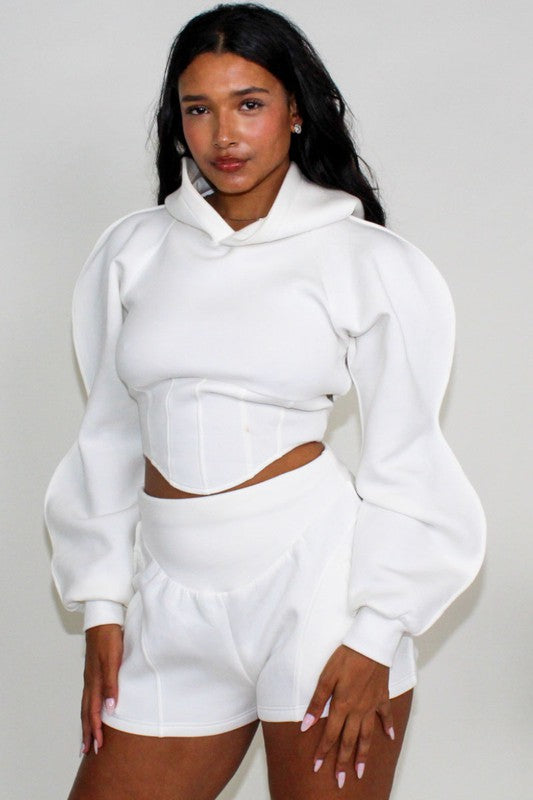 woman wearing a white hoodie and shorts set against a plain background