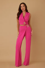 Woman wearing a bright pink outfit with a vest and pants on a beige background