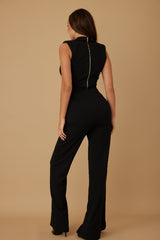 Woman wearing a black pant suit with gold zipper in back against a beige background