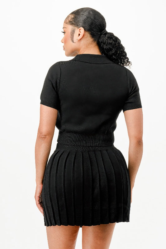 back view of woman wearing a black pleated skirt and black top on a white background