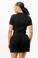 back view of woman wearing a black pleated skirt and black top on a white background