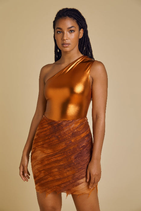 Woman wearing a bronze one-shoulder top and skirt against a beige background