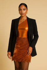 Woman wearing a black blazer over a copper skirt set on a beige background