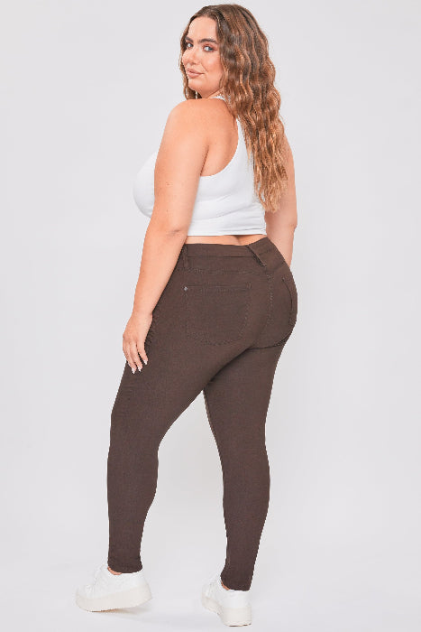 Woman wearing brown leggings and a white crop top on a plain background