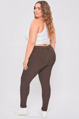 Woman wearing brown leggings and a white crop top on a plain background
