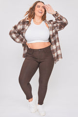 Woman wearing a plaid shirt, white crop top, and brown pants on a white background