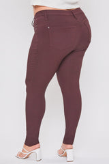 A person shown from the back wearing slim-fit burgundy leggings and white heeled sandals against a light gray studio background.