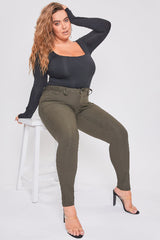 Woman sitting on a stool wearing a black top and green pants against a white background