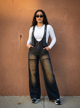 Person wearing black overalls and white shirt against a brown wall