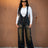 Woman wearing black overalls and sunglasses against a brown wall