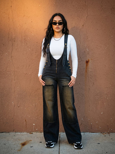 Woman wearing black overalls and sunglasses against a brown wall