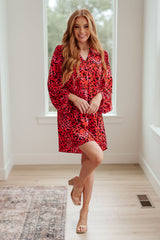 Woman wearing a red leopard print dress in a bright room with large windows.