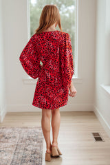 Woman wearing a red leopard print dress in a bright room.