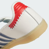 Close-up of a white leather sneaker showing the heel and side profile, featuring a red heel counter, white contrast stitching, blue side stripes, and a translucent gum sole.