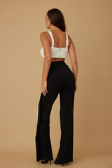 Woman wearing a white crop top jumpsuit with black flared pants on a beige background