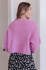Woman wearing a pink knitted sweater and floral skirt indoors.