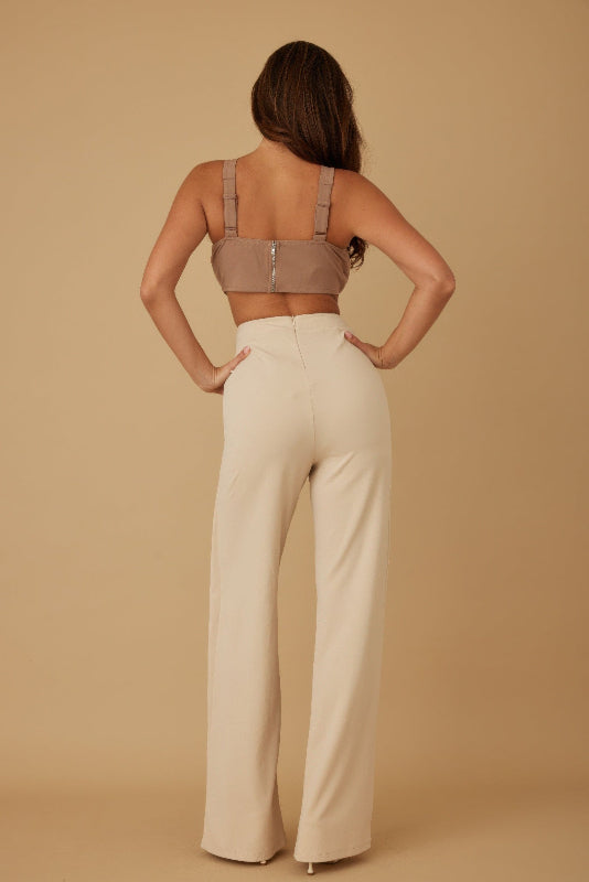 Woman wearing a beige top and wide-leg pants against a beige background back view