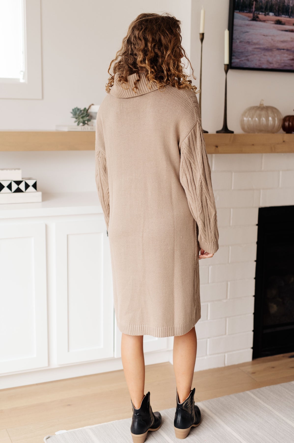 Woman wearing a beige sweater dress standing in a living room.