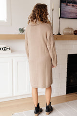 Woman wearing a beige sweater dress standing in a living room.