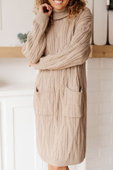Person wearing a beige cable knit sweater dress indoors.