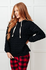 Woman wearing a black textured hoodie and red plaid pants against a white wall.