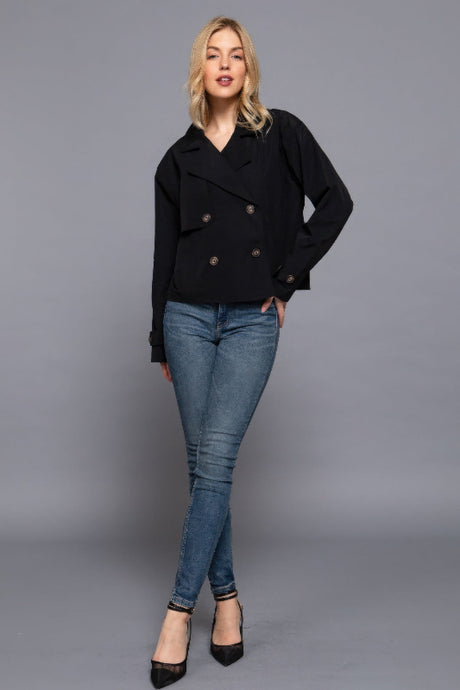 Woman wearing a black coat and blue jeans on a gray background
