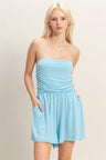 Woman wearing a light blue strapless romper against a plain background