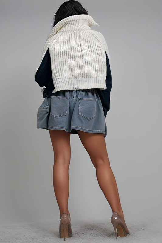 Person wearing a white knit sweater over a black top with a denim skirt on a gray background
