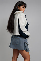 Woman wearing a white knit sweater and denim skirt on a gray background