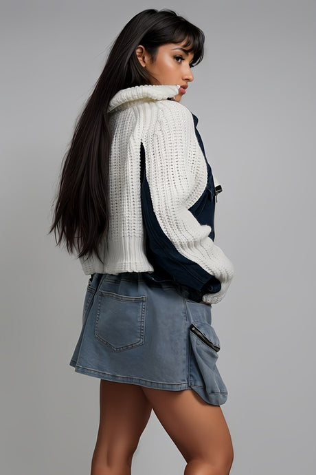 Woman wearing a white knit sweater and denim skirt on a gray background