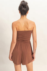 Woman wearing a brown strapless romper against a plain background